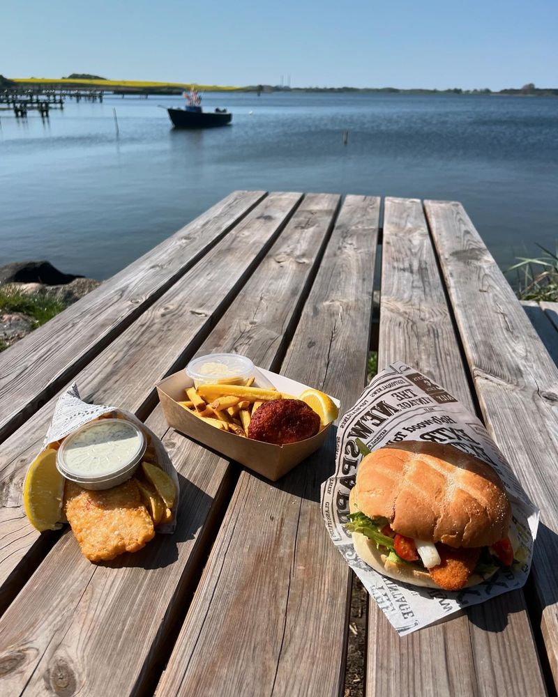 Fiskeburger, fiskefilet og pommes frites på et træbord ved vandet