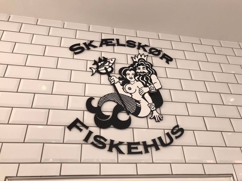 Skælskør Fiskehus-logoet på en hvid flisevæg
